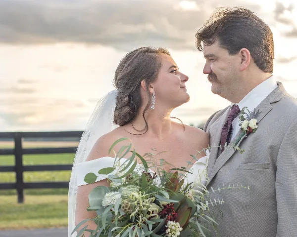 A bride and groom looking at each other outdoors, with the bride holding a bouquet.