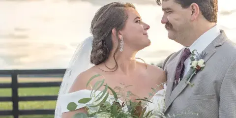A bride and groom looking at each other outdoors, with the bride holding a bouquet.