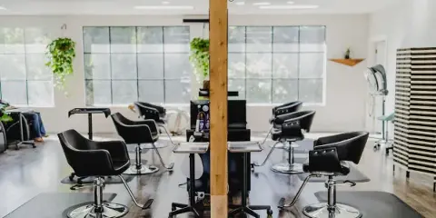 Interior view of a modern hair salon featuring black styling chairs, mirrors, and a central wooden pillar with plants.