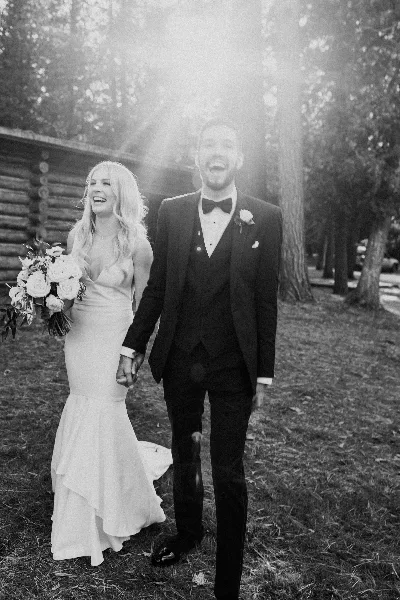 Black-and-white photo of a bride and groom walking hand-in-hand outdoors, with the bride holding a bouquet.