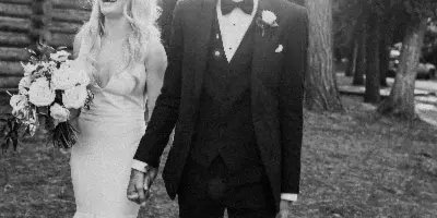 Black-and-white photo of a bride and groom walking hand-in-hand outdoors, with the bride holding a bouquet.