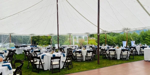 Interior view of a large white event tent set up on a lawn with round tables, chairs, and a wooden dance floor.