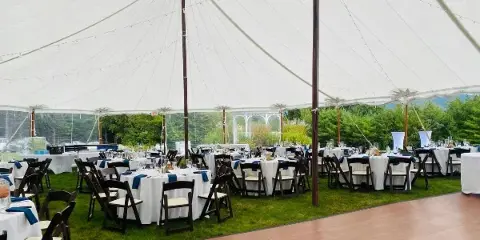 Interior view of a large white event tent set up on a lawn with round tables, chairs, and a wooden dance floor.