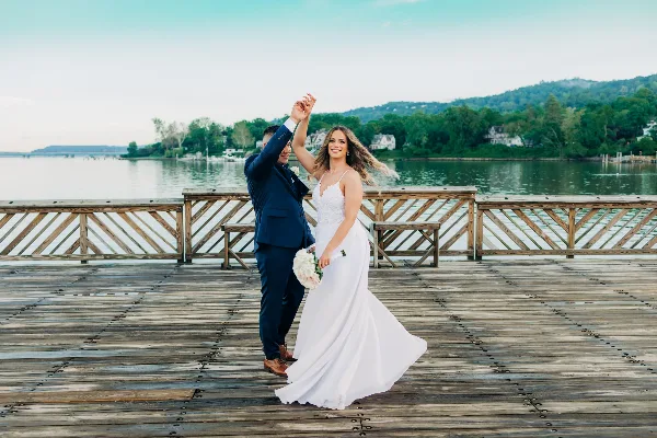 A bride and groom dancing on a wooden dock with a lake and hills in the background.