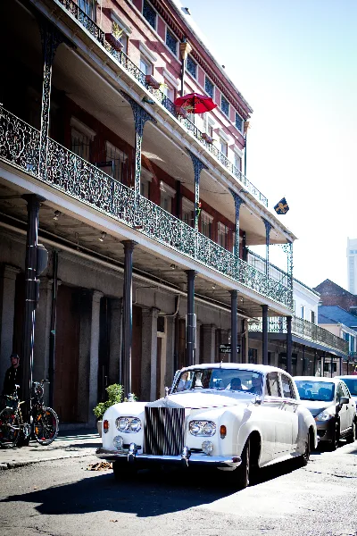 A white classic Rolls-Royce wedding car parked on a street in front of a historic building with ornate iron balconies.