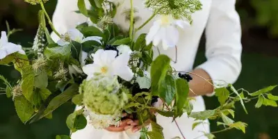 A bride in a white off-the-shoulder gown holding a lush bouquet of white flowers and greenery.