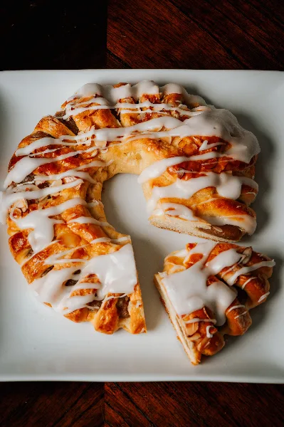 A braided pastry with white icing on a white plate