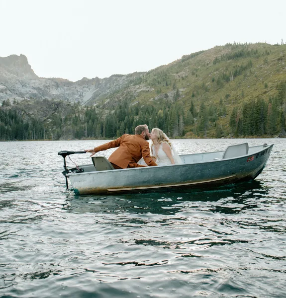 A bride and groom kissing in a small boat on a mountain lake.