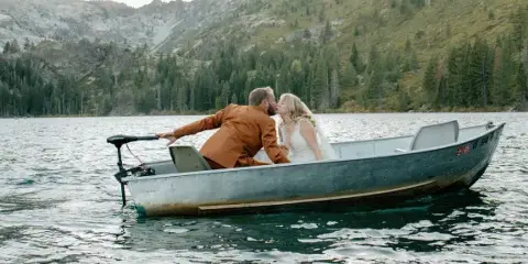 A bride and groom kissing in a small boat on a mountain lake.