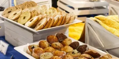A catering buffet table featuring trays of bagels, muffins, and pastries with serving tongs.