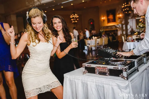 A professional DJ operating a turntable setup at a wedding reception while a guest dances nearby.