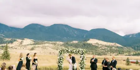 Outdoor wedding ceremony with a floral arch, wedding party, and guests in a Montana mountain setting.