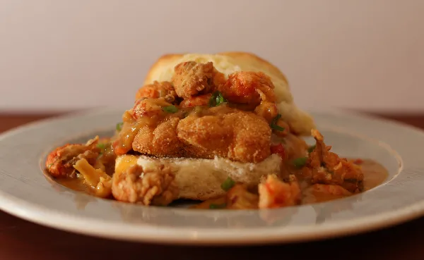 A biscuit sandwich topped with fried shrimp and gravy on a white plate.