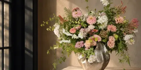 A lush floral arrangement featuring pink and white flowers in a metallic vase on a marble surface.