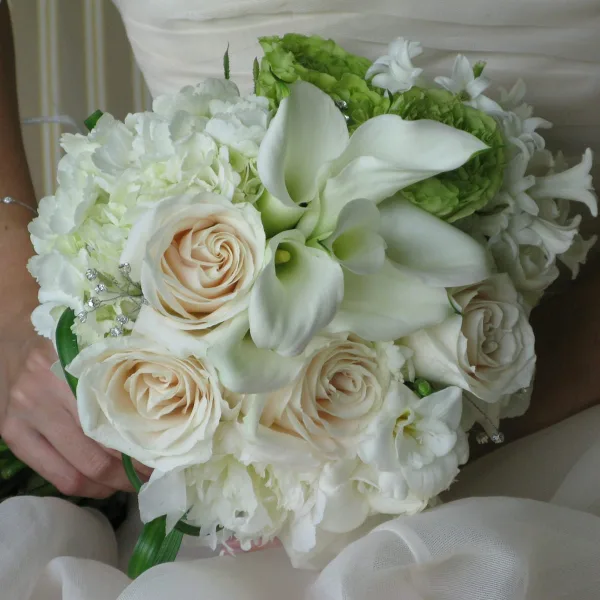 A bride holding a white bridal bouquet featuring roses, calla lilies, and hydrangea.