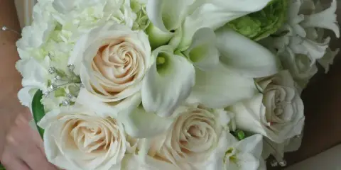 A bride holding a white bridal bouquet featuring roses, calla lilies, and hydrangea.