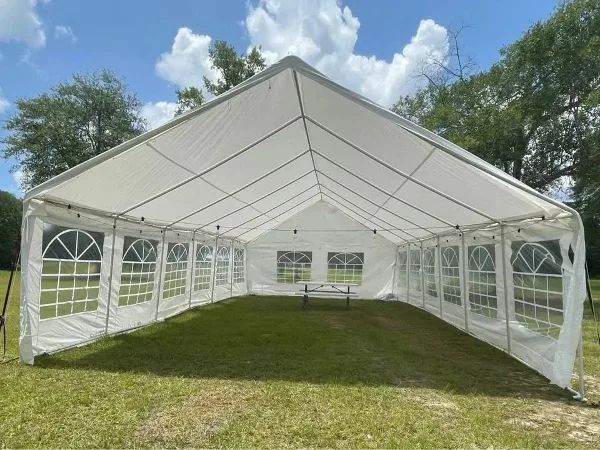 A large white event tent with windowed walls set up on a grassy lawn under a blue sky.
