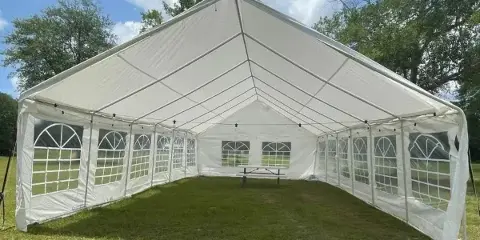 A large white event tent with windowed walls set up on a grassy lawn under a blue sky.