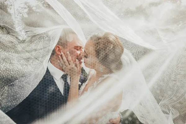 A bride and groom sharing a kiss, framed by a flowing white veil.