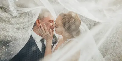 A bride and groom sharing a kiss, framed by a flowing white veil.