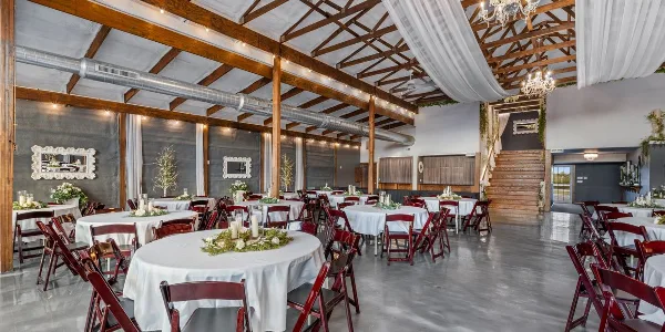 Interior view of a large wedding venue featuring round tables, a grand staircase, and exposed wooden beams.
