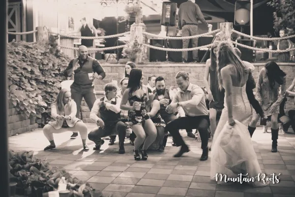 A black and white photograph of a wedding reception dance floor where a DJ is performing and guests are dancing.