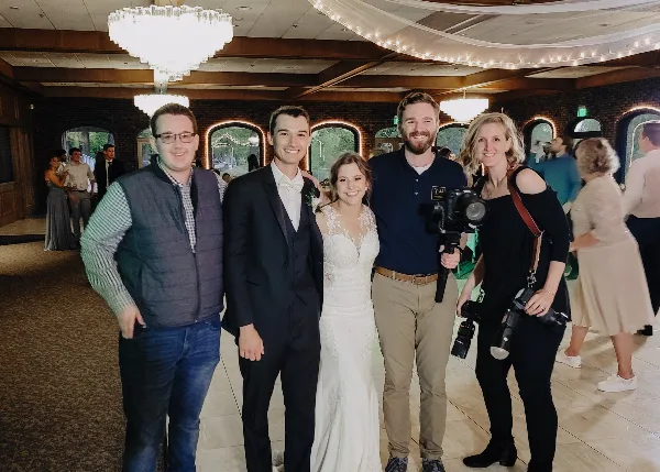 A wedding photography team posing with a bride and groom in a banquet hall.