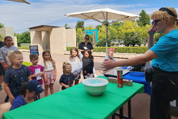 Outdoor view of the Oklahoma Hall of Fame venue grounds with a group of children and an instructor at a table under an umbrella.