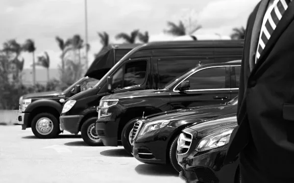 A row of black luxury vehicles, including a stretch SUV and a shuttle van, parked in a lot.