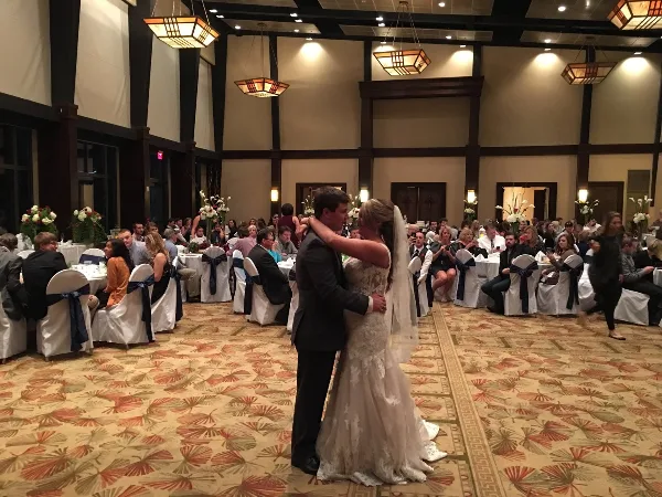 A bride and groom dancing in a wedding reception hall with guests seated at tables.