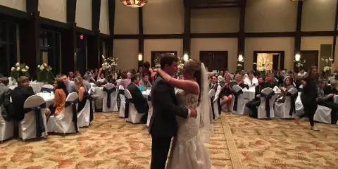 A bride and groom dancing in a wedding reception hall with guests seated at tables.