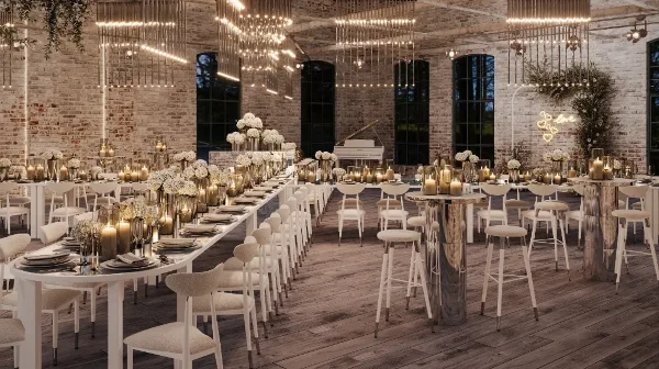 Styled event venue interior with long white banquet tables, upholstered chairs, bar stools, candles, floral centerpieces, and hanging light installations.