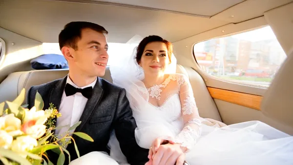 A bride and groom sitting together in the back seat of a luxury car.