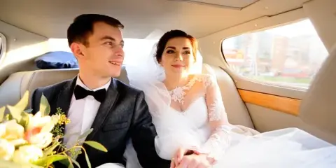 A bride and groom sitting together in the back seat of a luxury car.