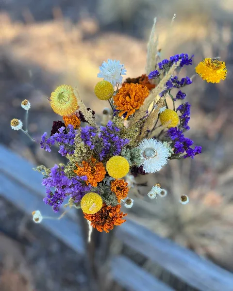 A colorful dried flower bouquet featuring purple, orange, and yellow blooms arranged in a vase.