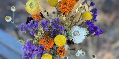 A colorful dried flower bouquet featuring purple, orange, and yellow blooms arranged in a vase.