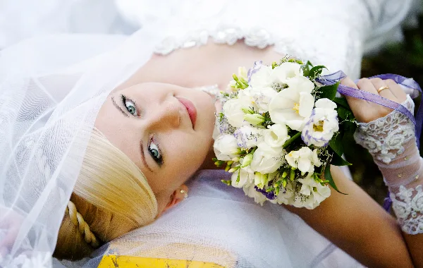 A bride in a white wedding dress and veil holding a bouquet of white and purple flowers.