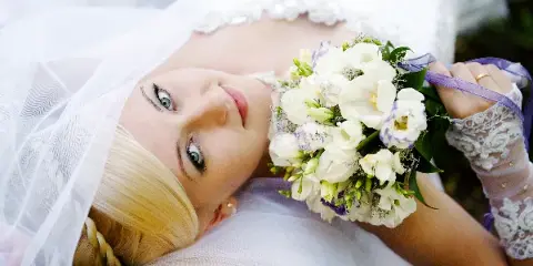 A bride in a white wedding dress and veil holding a bouquet of white and purple flowers.