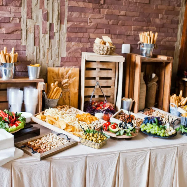 A catering buffet table featuring a variety of snacks, dips, and appetizers arranged on wooden crates and trays.