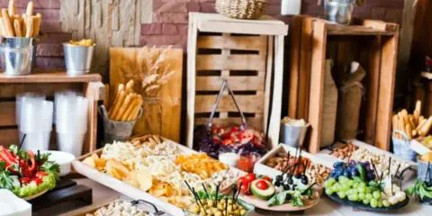 A catering buffet table featuring a variety of snacks, dips, and appetizers arranged on wooden crates and trays.