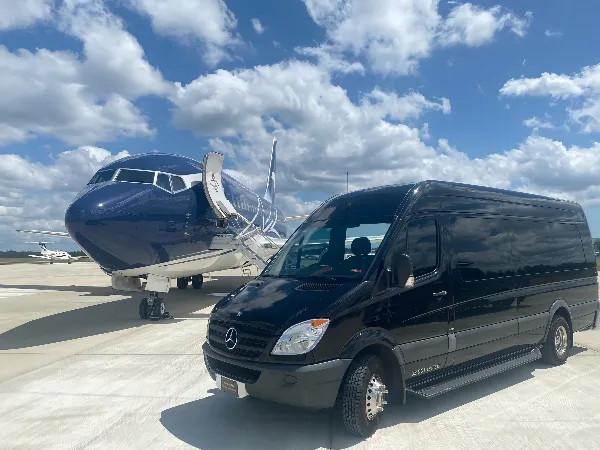 A black Mercedes-Benz Sprinter van parked on an airport tarmac next to a private jet.