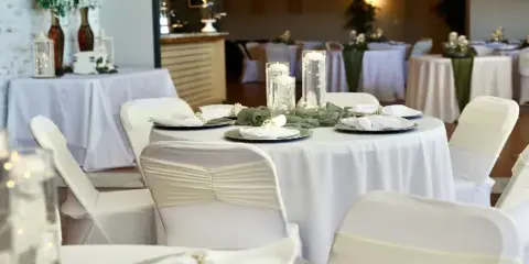 Interior view of a wedding reception hall with round tables, white linens, and string lights.