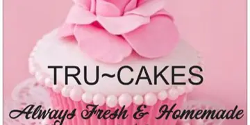 A pink cupcake topped with a large fondant rose, featuring the text 'TRU~CAKES Always Fresh & Homemade Bakery & Catering'.