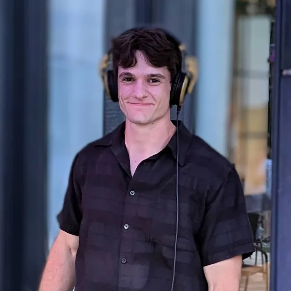 A young man wearing a black short-sleeved shirt and professional over-ear headphones.