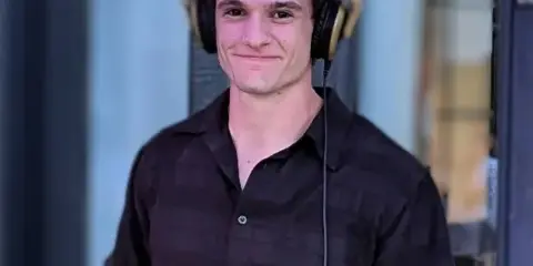 A young man wearing a black short-sleeved shirt and professional over-ear headphones.