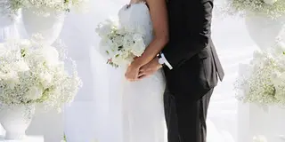 A bride and groom embracing at a wedding ceremony with white floral arrangements.