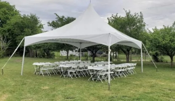 A white event tent set up on a grassy lawn with rows of white tables and chairs arranged underneath.