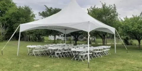 A white event tent set up on a grassy lawn with rows of white tables and chairs arranged underneath.