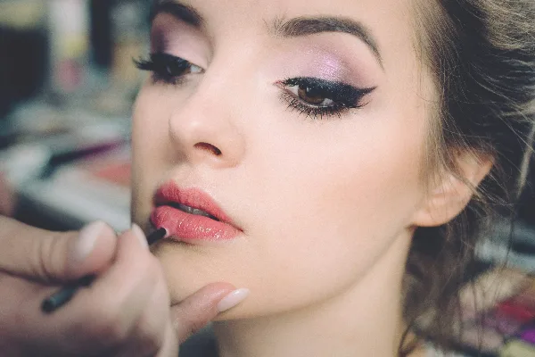 Close-up of a makeup artist applying lip liner to a client's face.