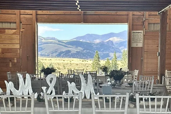 Interior of a wooden barn venue set up for a wedding reception with tables, chairs, and a mountain view through the open doorway.